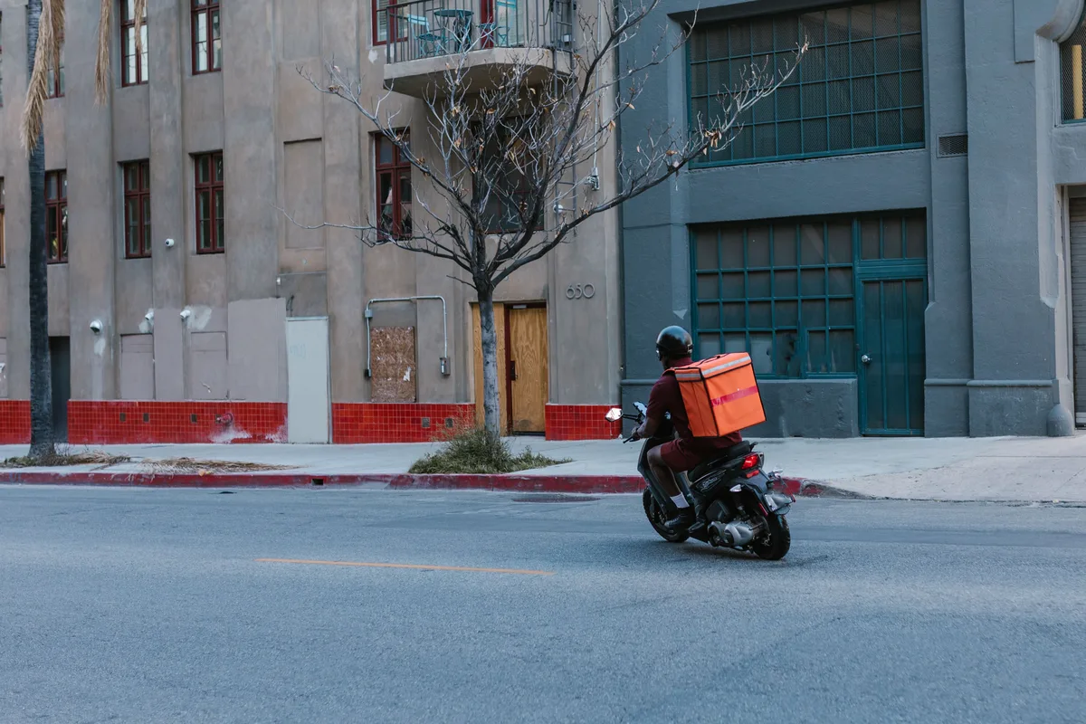 Street view of a courier on a motorcycle delivering a package in an urban setting