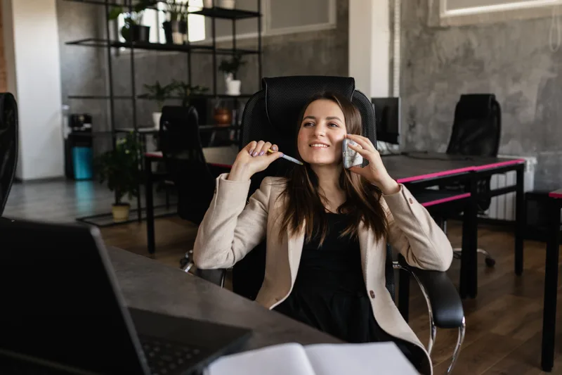 Smiling woman talking on her smartphone while sitting in a modern office setting